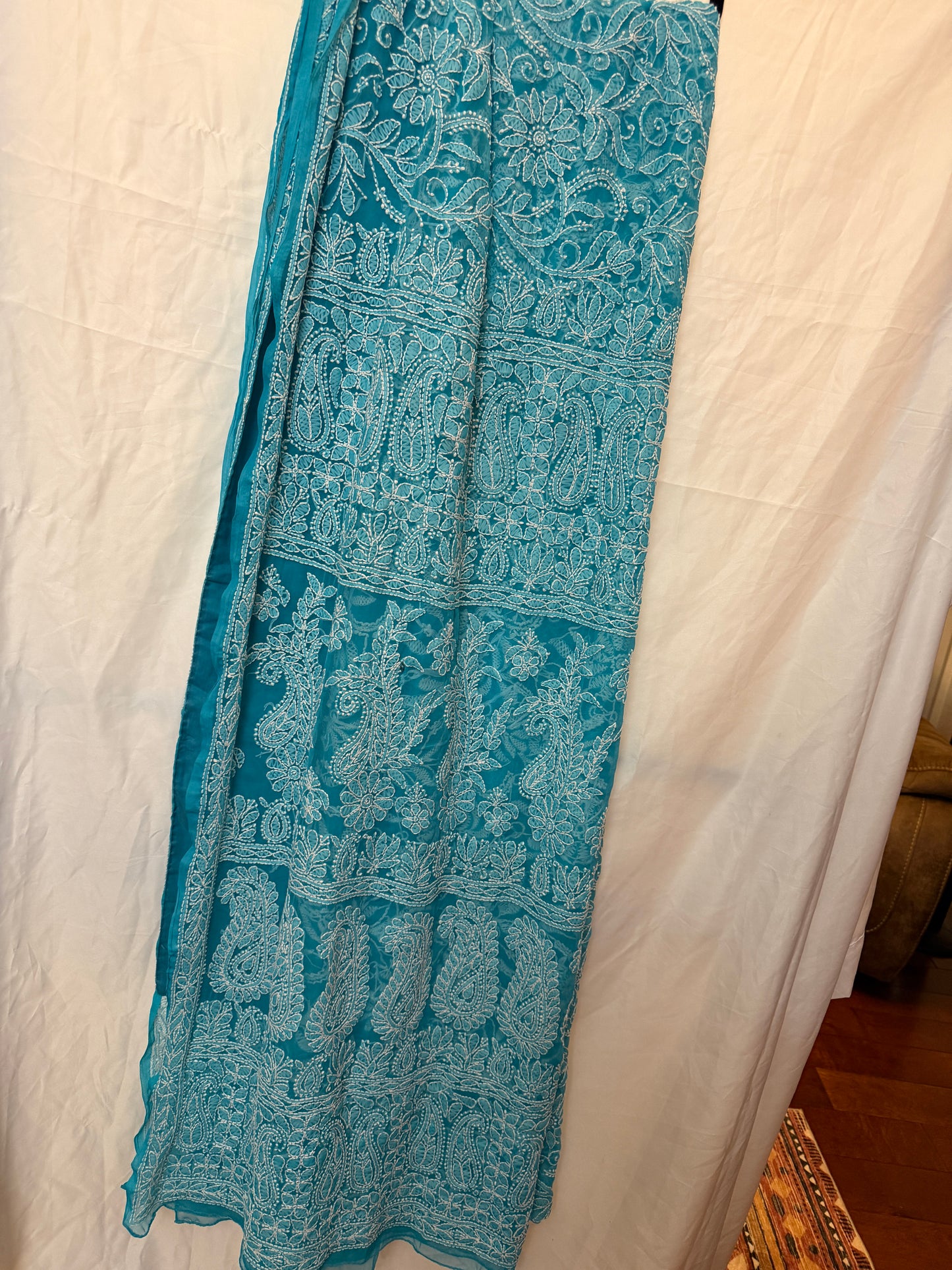Close-up of a sky blue pure georgette saree highlighting intricate white floral embroidery, paisley motifs, and an elegant embroidered border.