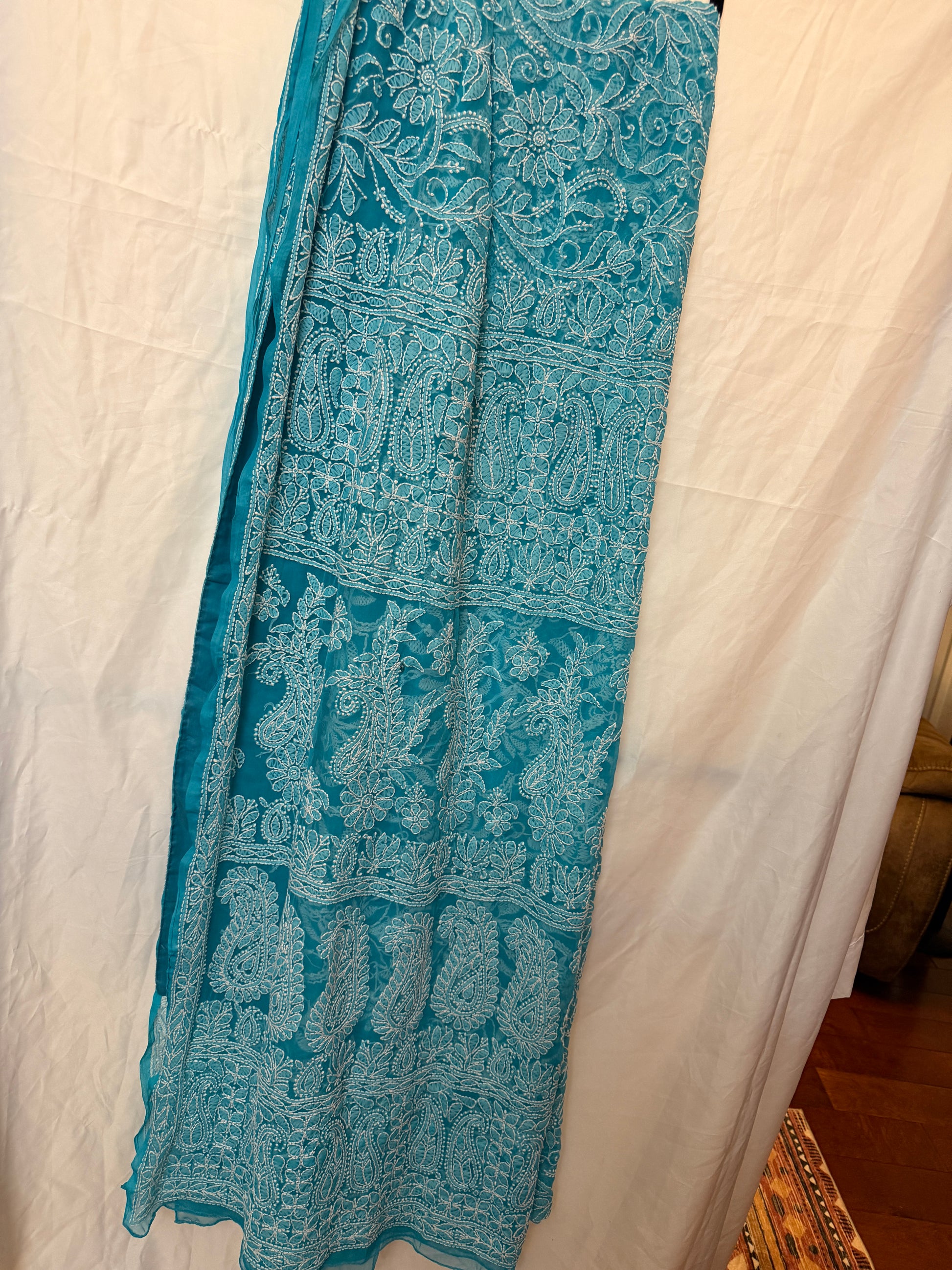 Close-up of a sky blue pure georgette saree highlighting intricate white floral embroidery, paisley motifs, and an elegant embroidered border.