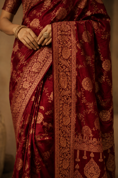 Close-up of maroon Dola silk saree displaying gold zari floral motifs and richly woven border.