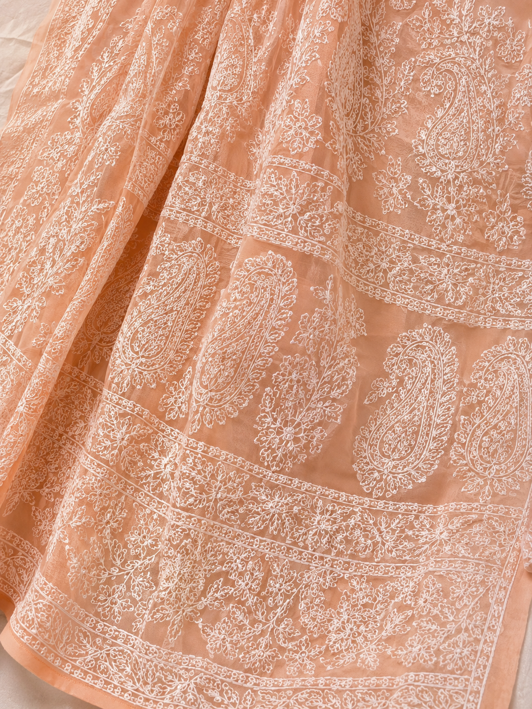 Close-up of a peach pure georgette saree with intricate white floral embroidery and paisley motifs, paired with a black embroidered blouse.