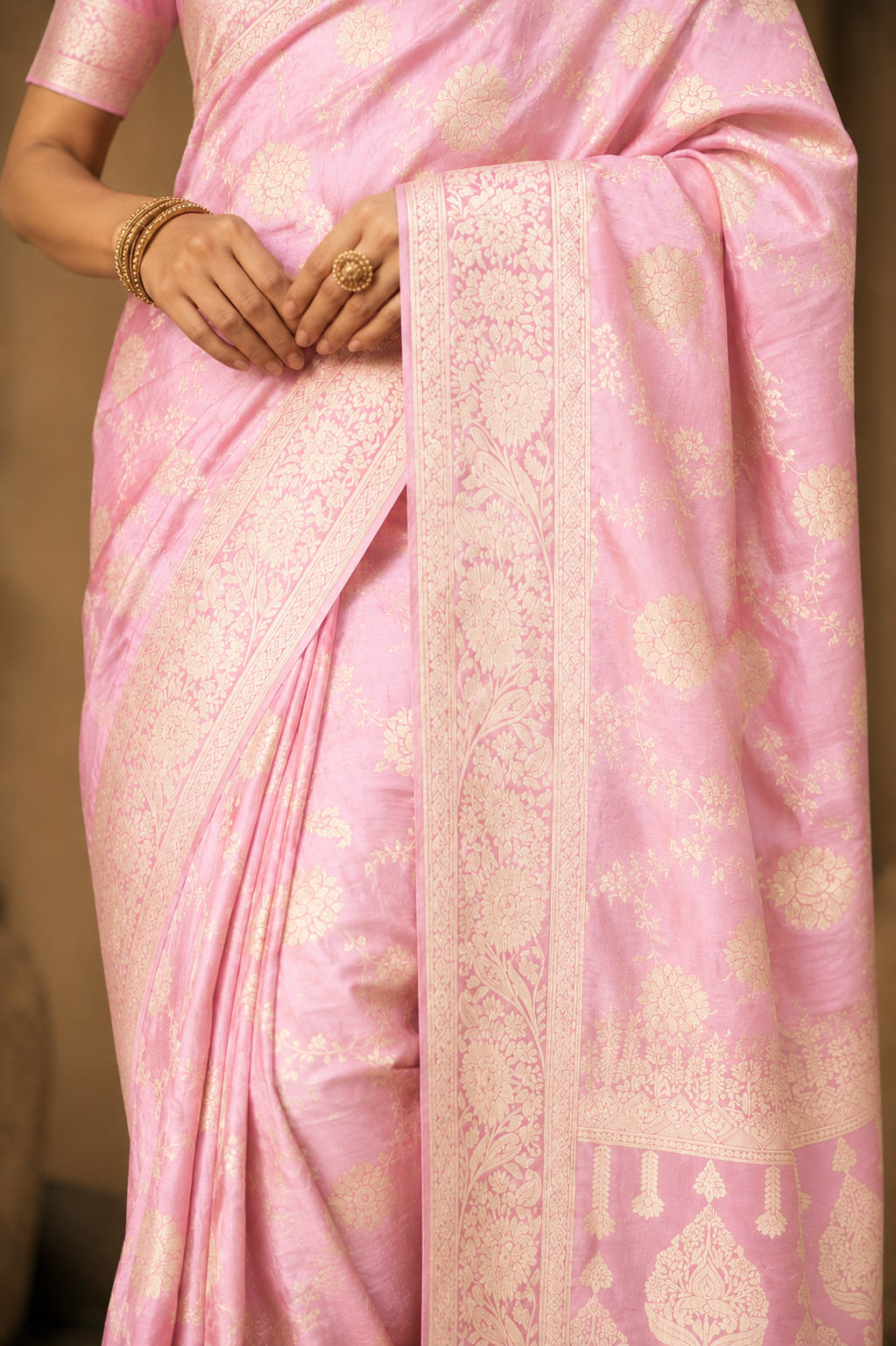 Close-up of baby pink Dola silk saree highlighting delicate gold zari floral motifs and woven border.