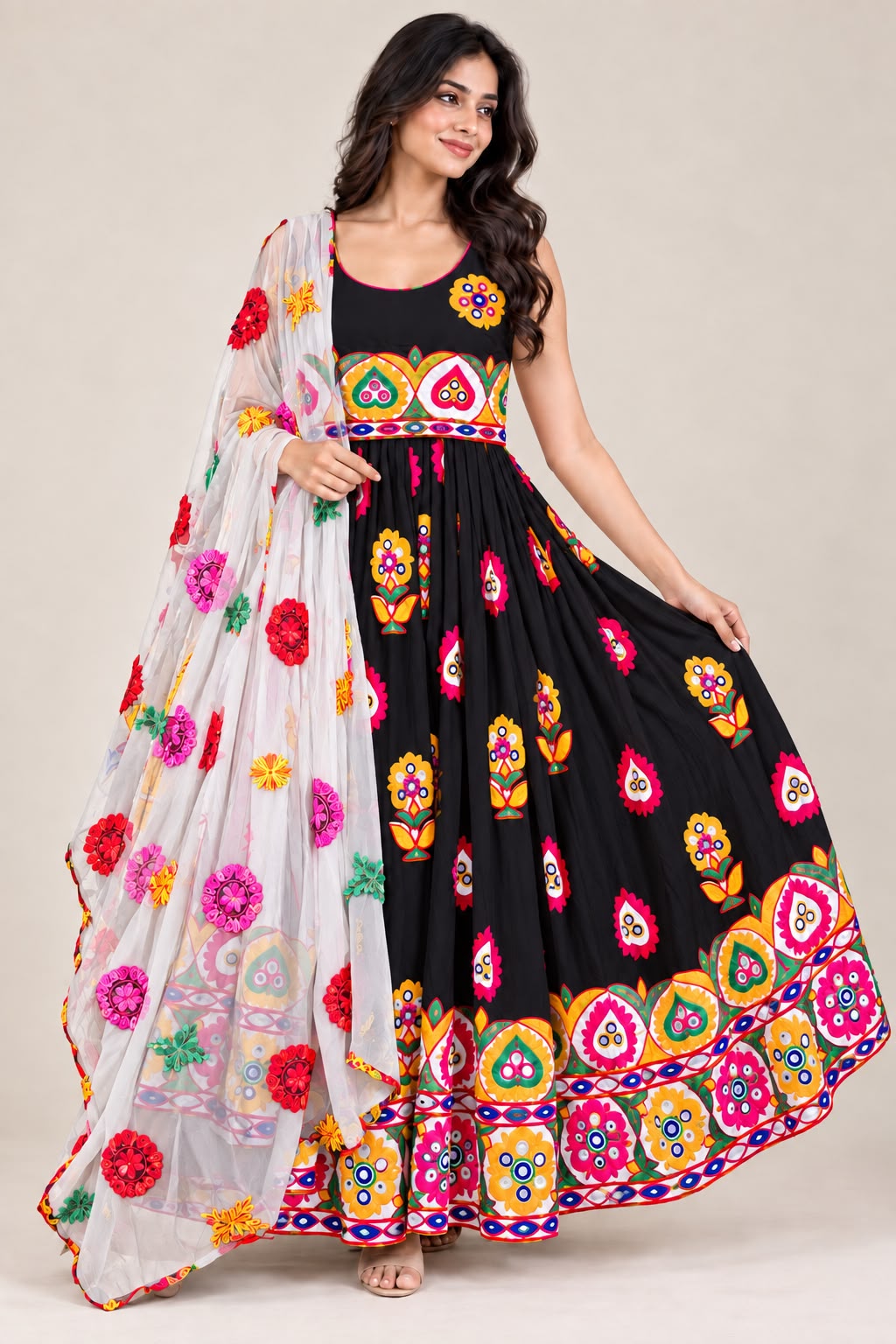 A woman modeling a black anarkali-style dress with colorful embroidered floral motifs and a white dupatta decorated with red, pink, yellow, and green floral embroidery, set against a plain beige studio background.