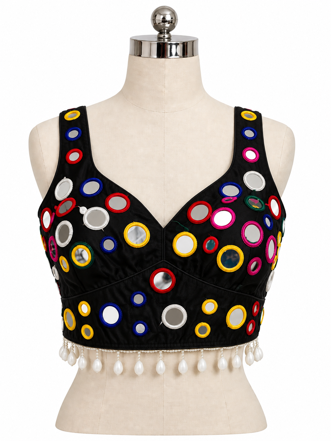 Black sleeveless crop top blouse with colorful circular mirror embellishments and white tassel fringe, displayed on a cream dress form mannequin against a white background.