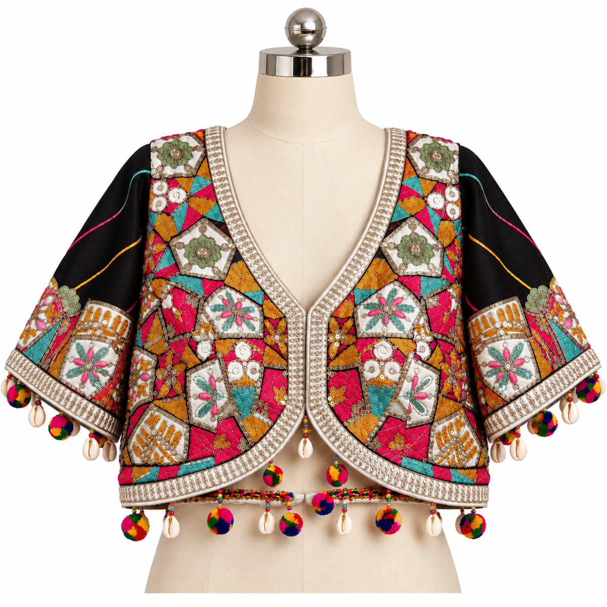 A cropped, short-sleeve blouse displayed on a cream dress form. The blouse features a black base with dense, colorful patchwork embroidery in pink, orange, teal, green, and gold, finished with a cream beaded V-neck trim and hanging multicolor tassels.