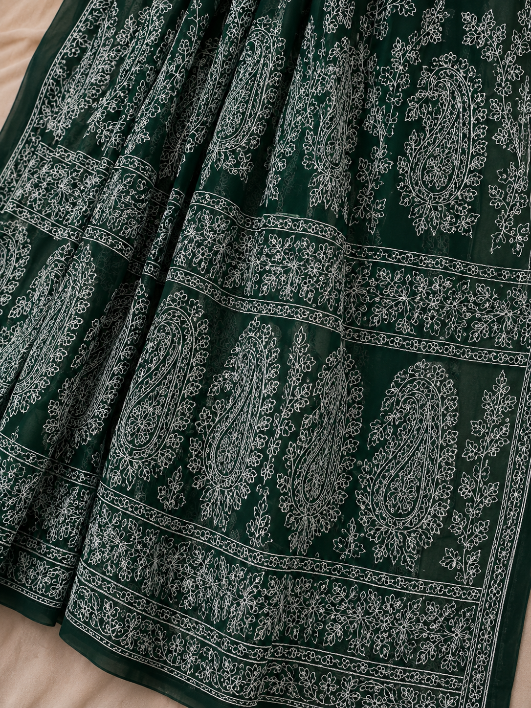 A dark green pure georgette saree with detailed white floral embroidery and paisley motifs, styled with a matching embroidered blouse.