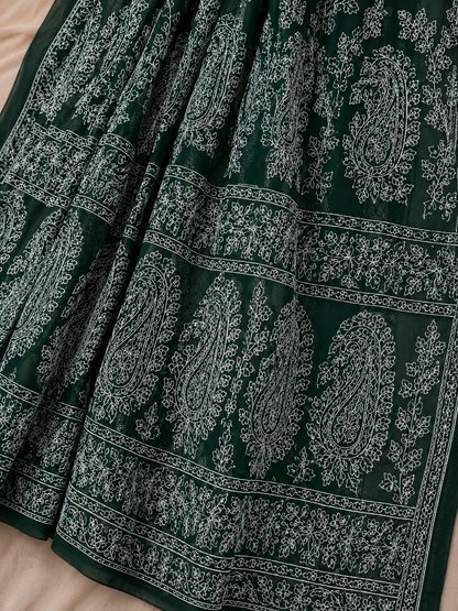 A dark green pure georgette saree with detailed white floral embroidery and paisley motifs, styled with a matching embroidered blouse.