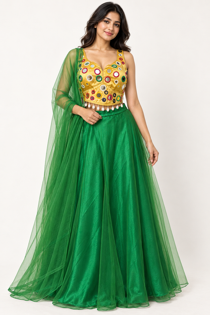 A woman modeling a traditional Indian formal gown with a bright green skirt and a heavily embellished gold mirror-work bodice, set against a plain white studio background.