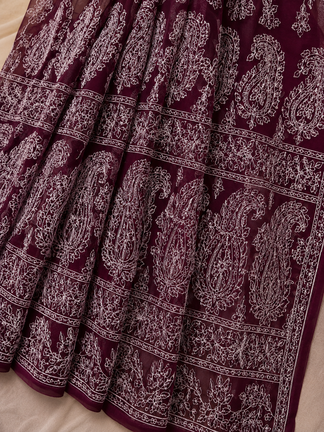 Close-up of a maroon pure georgette saree featuring delicate white floral embroidery, paisley motifs, and fine embroidered border detailing.