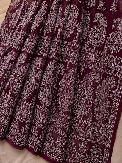 Close-up of a maroon pure georgette saree featuring delicate white floral embroidery, paisley motifs, and fine embroidered border detailing.