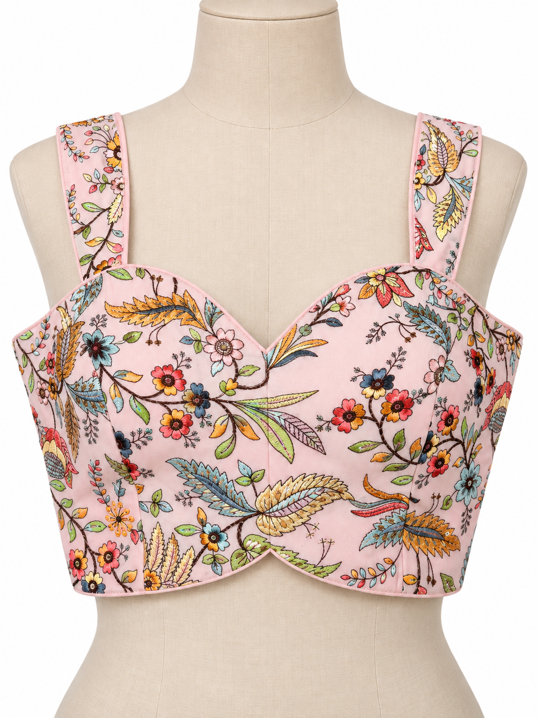 A pink floral bustier top displayed on a beige mannequin torso. The top features a sweetheart neckline, structured underwire cups, and wide shoulder straps, decorated with a vibrant multicolor botanical print of flowers, leaves, and birds.