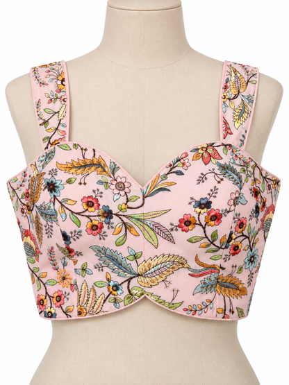 A pink floral bustier top displayed on a beige mannequin torso. The top features a sweetheart neckline, structured underwire cups, and wide shoulder straps, decorated with a vibrant multicolor botanical print of flowers, leaves, and birds.