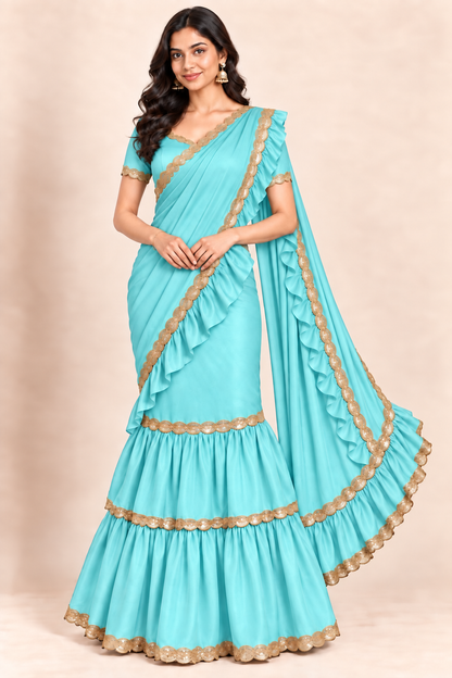 A woman modeling a turquoise blue saree with gold zari embroidery and ruffled detailing, set against a solid beige studio background.