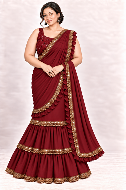 A woman modeling a deep maroon georgette lehenga choli suit with gold zari embroidery and scalloped borders, set against a light beige textured studio background.