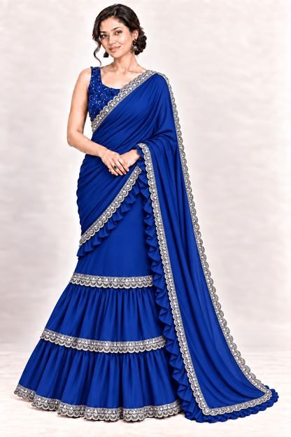 A woman modeling a royal blue georgette saree with intricate silver embroidery and ruffle details, set against a light beige studio background.