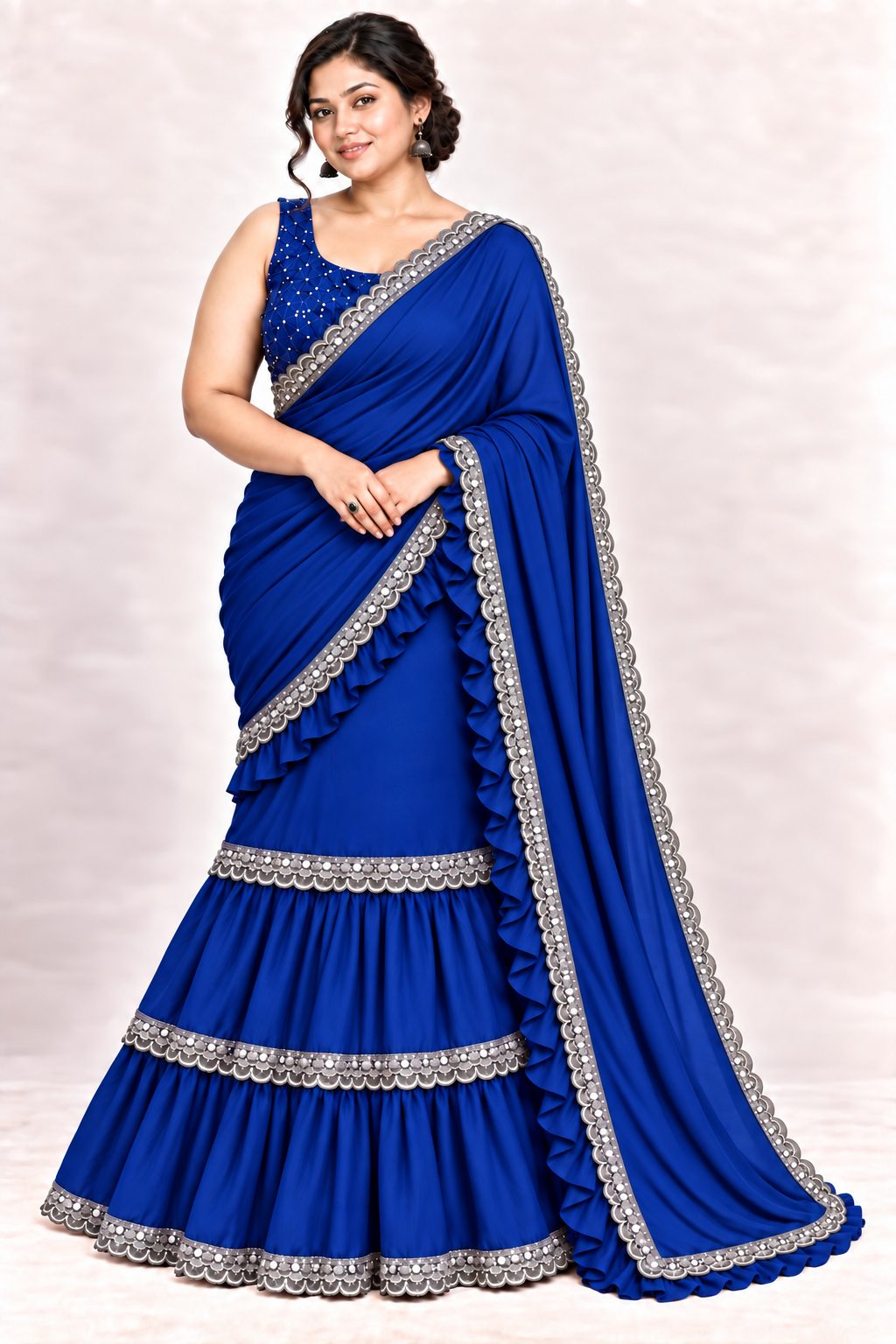 A woman modeling a royal blue georgette saree with silver embroidered borders and a matching blue embellished blouse, set against a light beige studio background.