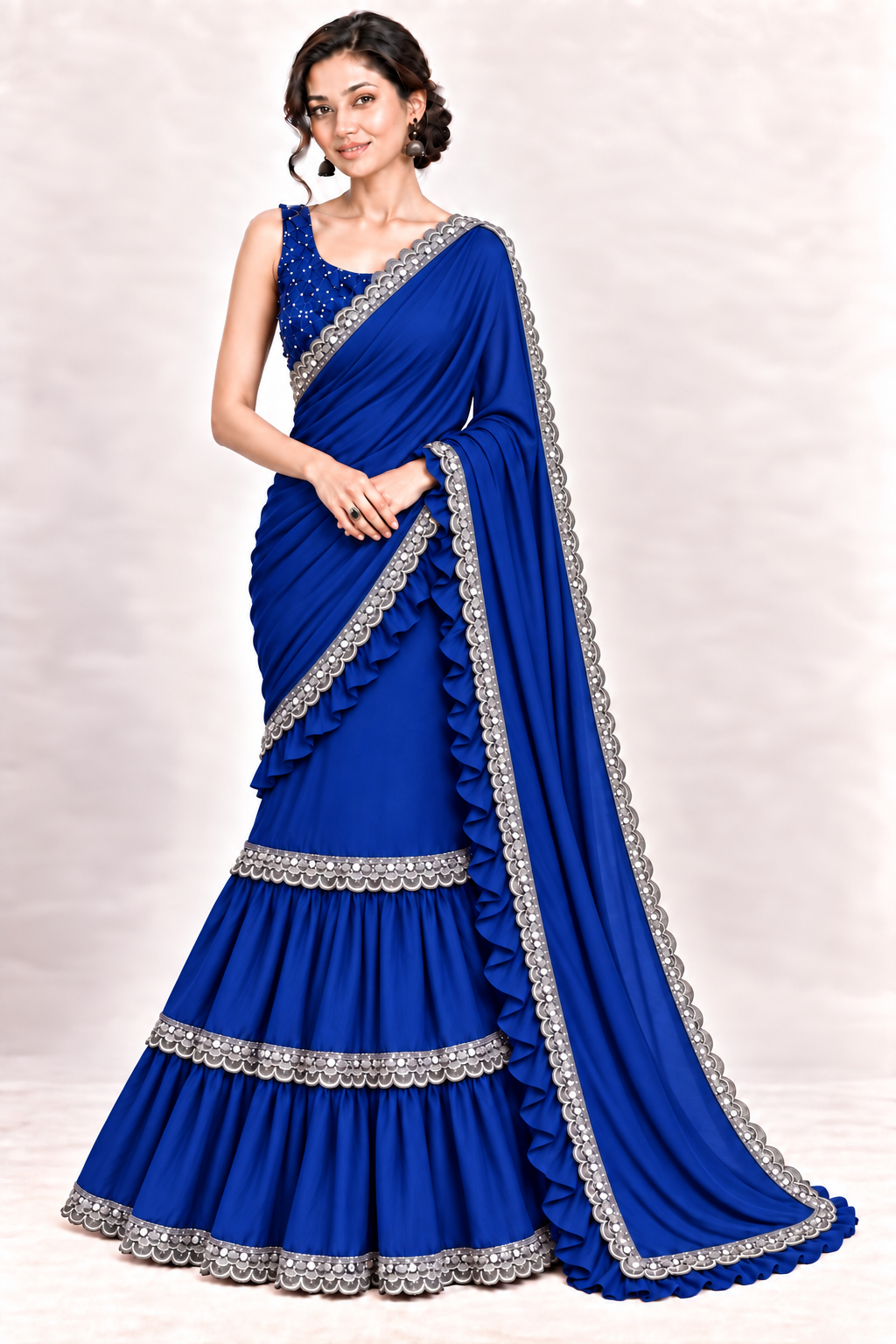 A woman modeling a royal blue georgette saree with silver embroidered borders and a matching embellished blouse against a light beige studio background.