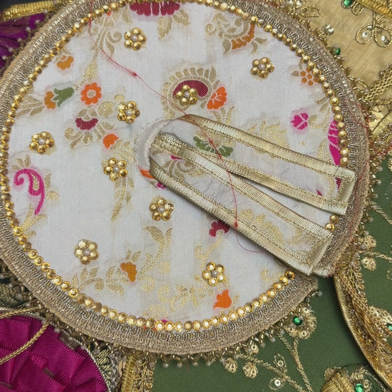Close-up of colorful Laddu Gopal poshak fabrics with traditional woven patterns and gold embellishments