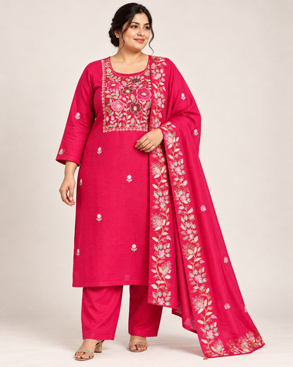 A woman modeling a bright pink Indian ethnic suit set featuring a kurta with floral embroidery, matching trousers, and a draped dupatta, set against a plain light beige background.