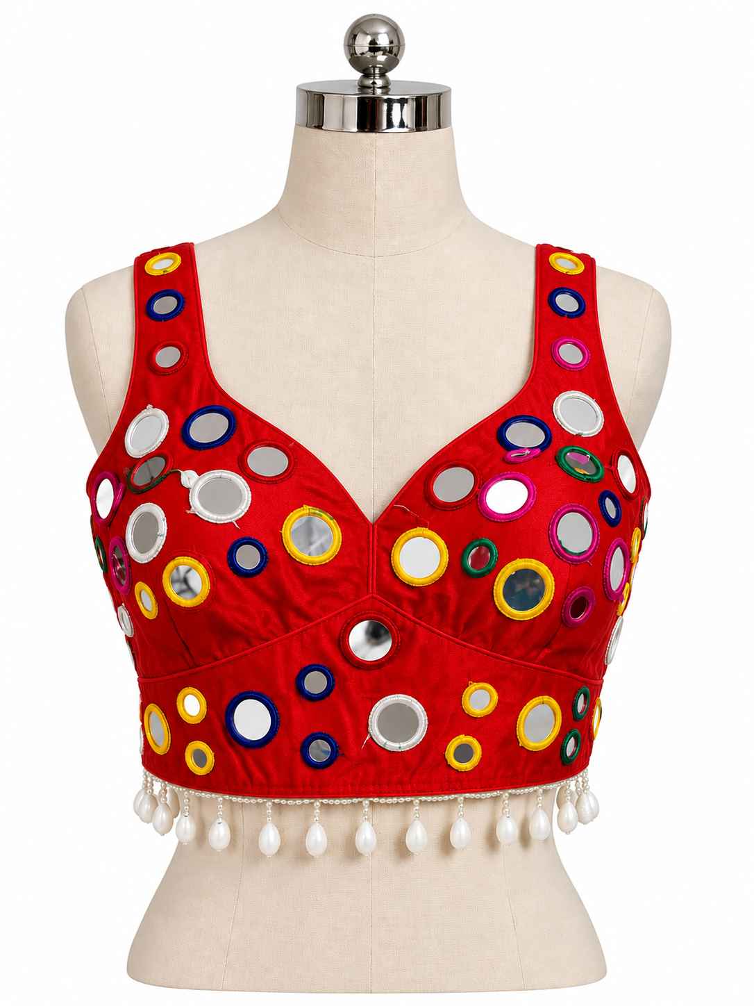 A red sleeveless crop top blouse with a V-neckline, decorated with colorful circular mirror work and white tassel fringe, displayed on a beige dress form mannequin against a white background.