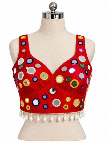 A red sleeveless crop top blouse with a V-neckline, decorated with colorful circular mirror work and white tassel fringe, displayed on a beige dress form mannequin against a white background.
