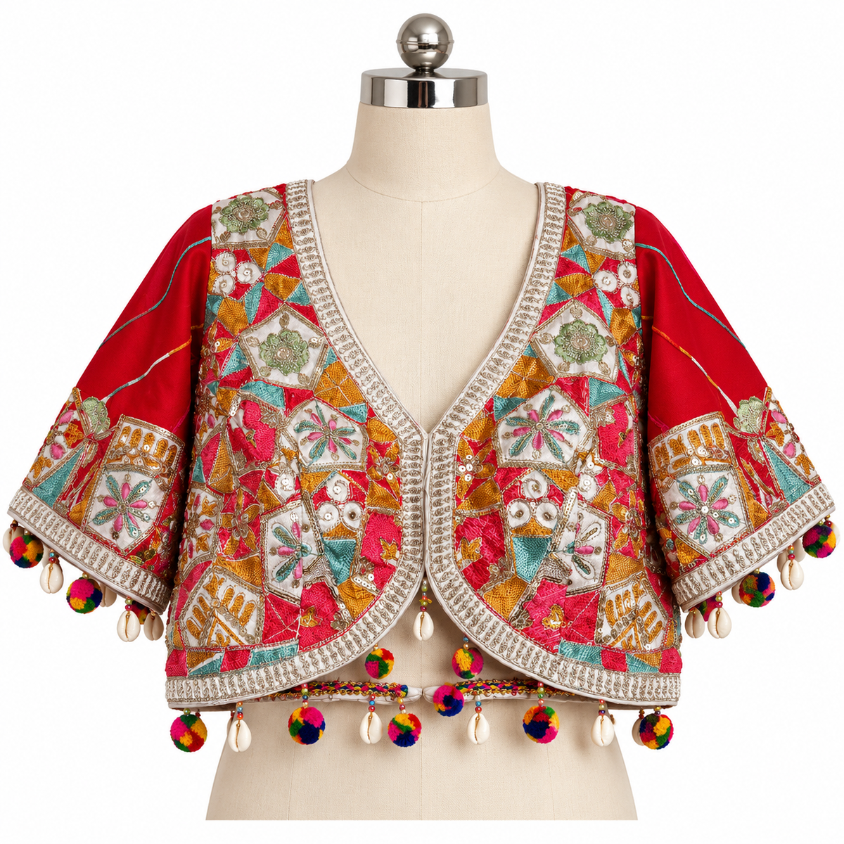 A red cropped embroidered jacket with multicolor geometric and floral embroidery, silver bead trim, and colorful pom-pom tassels, displayed on a cream dress form against a white background.