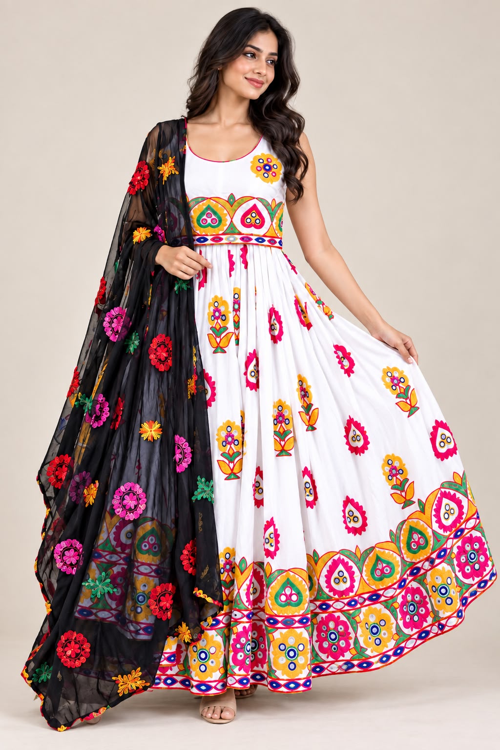 A woman models a white sleeveless maxi dress with colorful floral and geometric embroidery, paired with a black sheer dupatta featuring matching embroidered flowers, against a plain beige studio background.