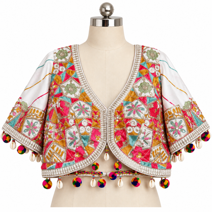 A white cropped bolero jacket with vibrant multicolor embroidery, bead borders, and colorful pom-pom tassels, displayed on a beige dress form mannequin against a white background.