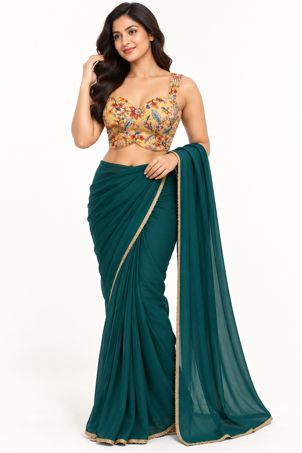 A woman modeling a dark teal green saree with a gold-trimmed border and a matching embroidered blouse. The blouse features a beige base with colorful floral patterns in red, blue, and yellow.
