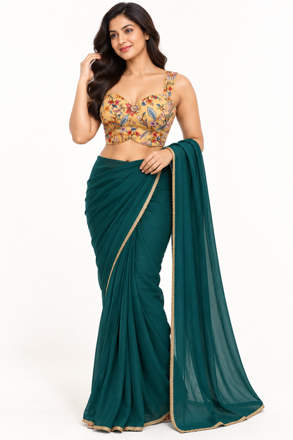 A woman modeling a dark teal green saree with a gold-trimmed border and a matching embroidered blouse. The blouse features a beige base with colorful floral patterns in red, blue, and yellow.