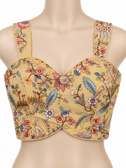 A mustard yellow bustier-style crop top with a colorful floral and bird print, displayed on a beige mannequin torso against a white background.